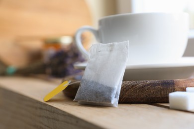 Tea bag and cup on wooden table indoors, closeup