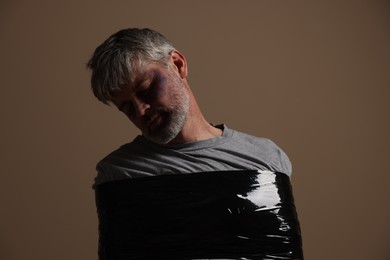Photo of Beaten man tied with duct tape on beige background. Hostage taking