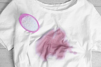 White t-shirt with stain and powdered detergent on wooden surface, top view. Hand washing laundry