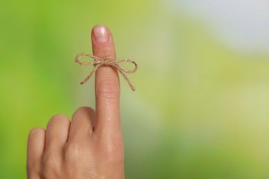 Woman showing index finger with tied bow as reminder on green blurred background, closeup. Space for text
