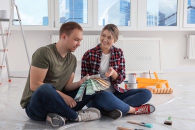 Photo of Happy couple with paint chips discussing interior details in apartment during repair