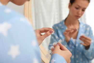 Photo of Teen girl applying acne healing patch near mirror in bathroom, focus on hands