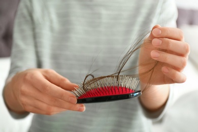 Woman holding brush with fallen long hair, closeup