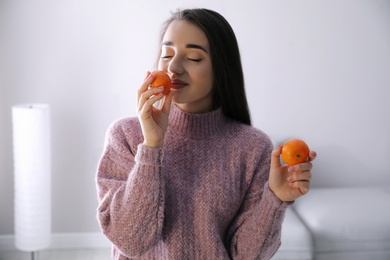 Happy young woman with fresh ripe tangerines at home