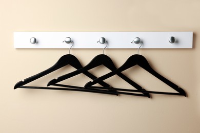 Rack with empty black clothes hangers on beige wall