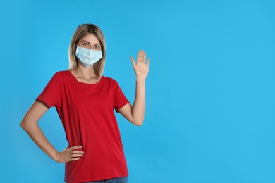 Woman in protective mask showing hello gesture on light blue background, space for text. Keeping social distance during coronavirus pandemic