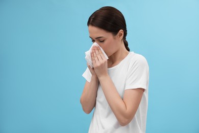 Woman blowing nose on light blue background. Cold symptoms