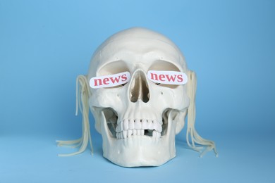Information and media warfare concept. Human skull with noodles and words News in eye sockets on light blue background