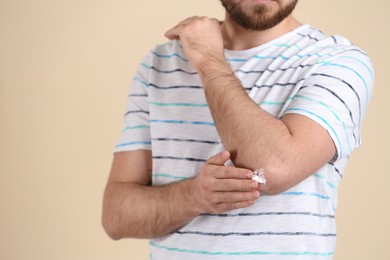 Man applying cream onto elbow on beige background, closeup. Space for text