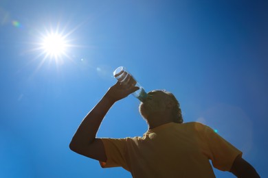 Senior man drinking water to prevent heat stroke outdoors, low angle view