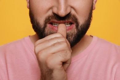 Man biting his nails on yellow background, closeup. Bad habit