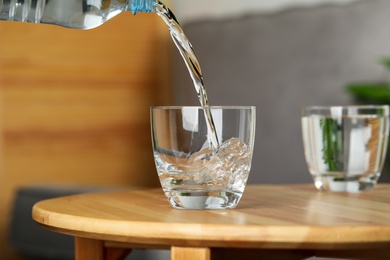 Pouring water from bottle into glass on wooden table indoors, space for text. Refreshing drink