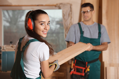 Professional carpenters with wooden plank in workshop