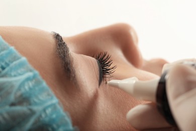 Photo of Young woman undergoing procedure of permanent eyeliner makeup on white background, closeup