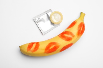 Condom and banana with lipstick kiss marks on white background, top view. Safe sex