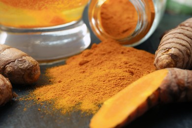 Photo of Glass cup of tasty tea, turmeric roots and powder on black table, closeup