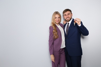Happy young business people with house key on light background, space for text