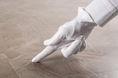 Person in white glove checking cleanliness of beige stone table, closeup