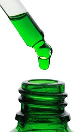 Photo of Dripping green facial serum from pipette into glass bottle on white background, closeup