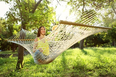 Photo of Young woman with hat resting in comfortable hammock at green garden