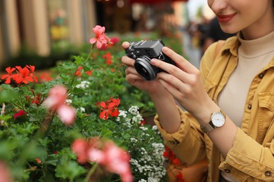 Young woman with camera taking photo of beautiful flowers on city street, closeup. Interesting hobby