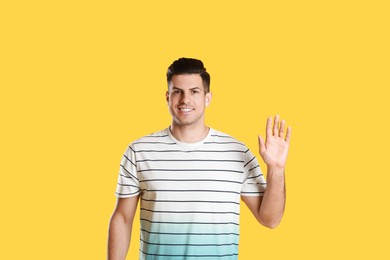 Photo of Cheerful man waving to say hello on yellow  background