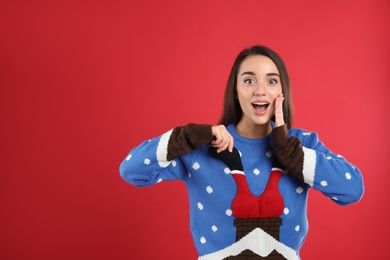 Surprised young woman in Christmas sweater on red background, space for text