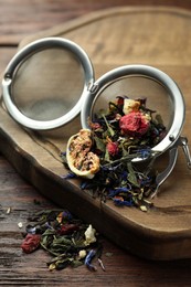Photo of Snap infuser with dried herbal tea leaves and fruits on wooden table, closeup