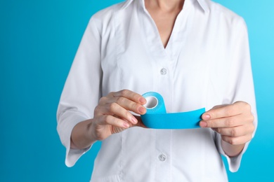Female doctor holding elastic therapeutic tape on color background, closeup. Medical object