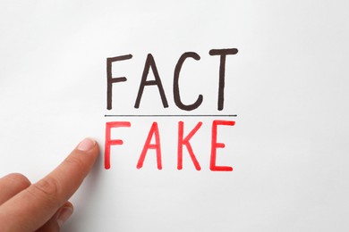 Woman pointing at words Fact and Fake on white background, top view