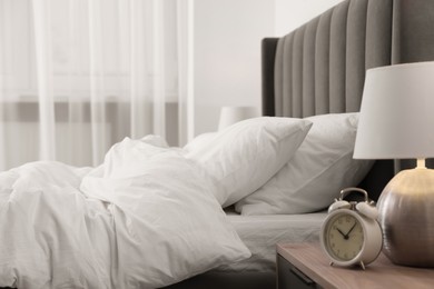 Photo of Lamp, alarm clock on bedside table and comfortable bed in light room. Stylish interior