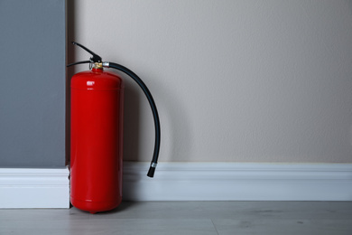 Fire extinguisher near light wall indoors. Space for text