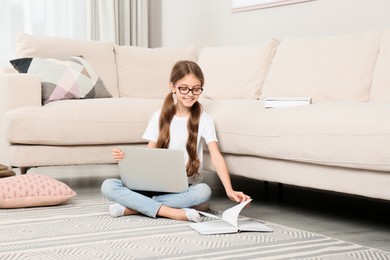 Girl with laptop and book sitting on floor at home