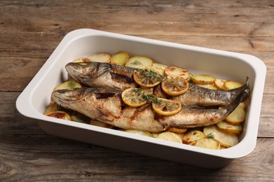 Photo of Baking tray with delicious baked sea bass fish and potatoes on wooden table