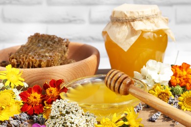 Delicious honey, combs and different flowers on wooden table near white brick wall