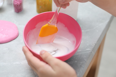 Little girl mixing ingredients with silicone spatula at table, closeup. DIY slime toy