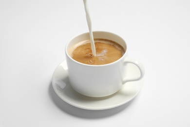 Pouring milk into cup of coffee on white background