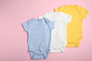 Child's bodysuits on pink background, flat lay