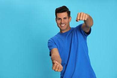 Happy man pretending to drive car on light blue background. Space for text