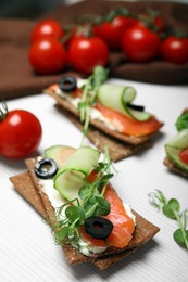 Tasty rye crispbreads with salmon, cream cheese and vegetables on white wooden table, closeup