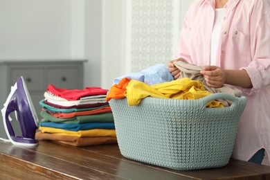 Woman with basket full of clean laundry at wooden table indoors, closeup
