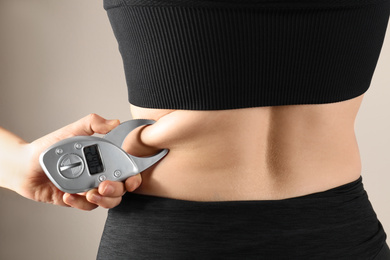 Nutritionist measuring woman's body fat layer with digital caliper on beige background, closeup