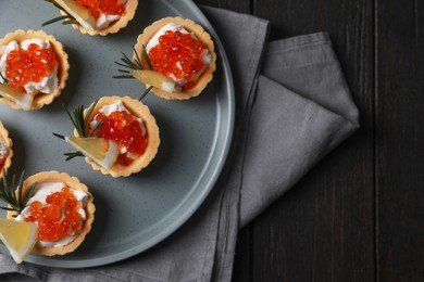 Photo of Delicious tartlets with red caviar and cream cheese served on wooden table, top view. Space for text
