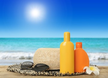 Bottles of skin sun protection products and beach accessories on wooden table against seascape. Space for design