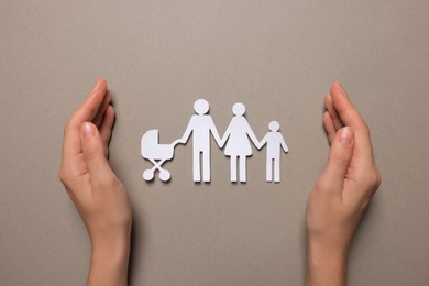 Photo of Woman protecting paper family figures on light grey background, top view. Insurance concept