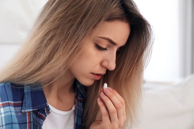 Upset young woman taking abortion pill on blurred background, closeup