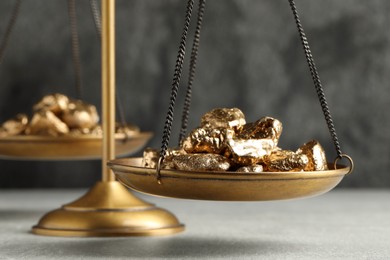 Photo of Vintage scales with gold nuggets on light table against grey background, closeup
