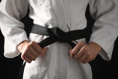 Man in keikogi with black belt on dark background, closeup. Martial arts uniform