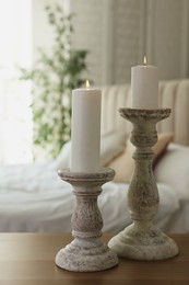 Photo of Pair of beautiful candlesticks on wooden table in bedroom