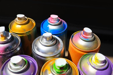 Used cans of spray paint on dark background, closeup. Graffiti supplies